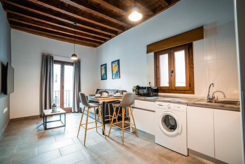 A compact kitchen with a washing machine, a dining area with a table and chairs, and a window with curtains.