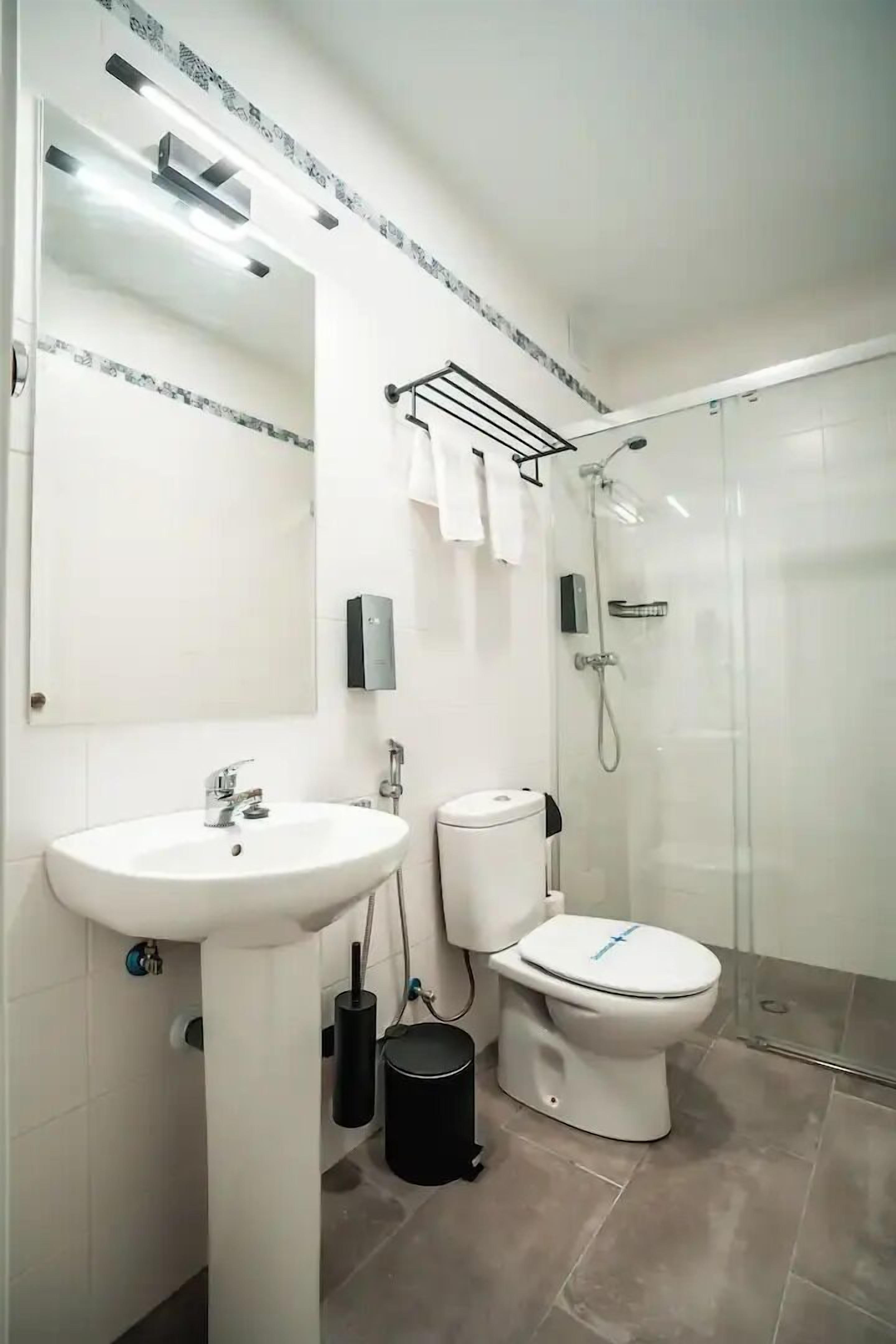 Un baño moderno con lavamanos blanco, inodoro y cabina de ducha con mampara de vidrio.