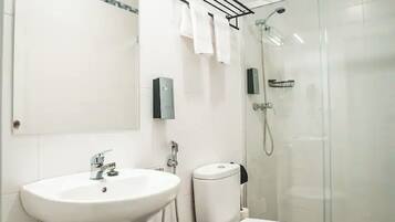 Un baño moderno con lavamanos blanco, inodoro y cabina de ducha con mampara de vidrio.