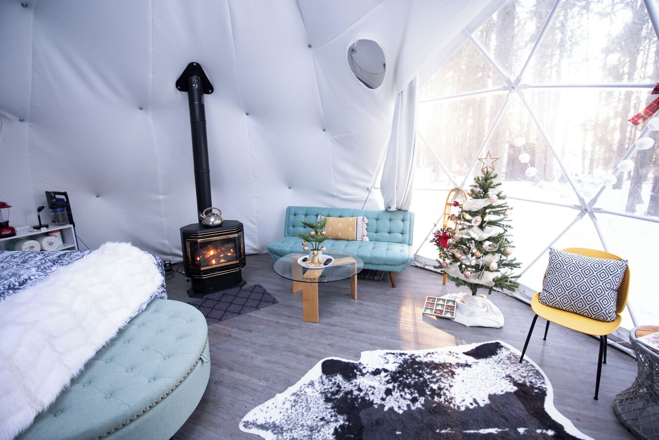 A cozy interior with a sofa, a small table, a Christmas tree, and a wood-burning stove.