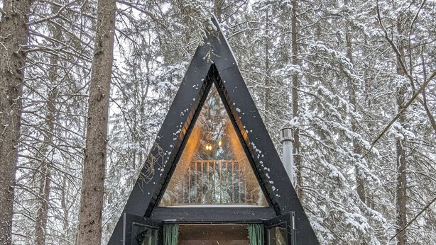 A cabin with a triangular roof, a central fire pit, and four Adirondack chairs. - The Hawthorn A-frame Cabin (Alberta Beach)