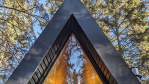 A triangular cabin with a balcony, a window, and a view of trees. - The Hawthorn A-frame Cabin (Alberta Beach)