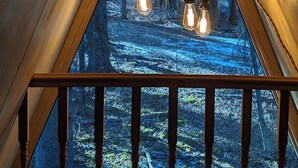 A triangular attic window with a view of a forested area. - The Hawthorn A-frame Cabin (Alberta Beach)