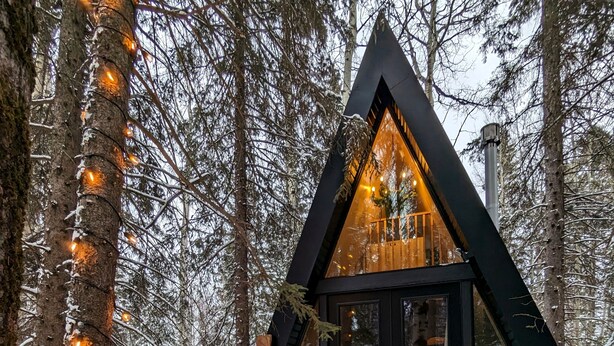 A cozy cabin with a fireplace, surrounded by snow-covered trees and wooden deck furniture. - The Fern A-frame Cabin (Alberta Beach)