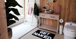 Een badkamer met een houten wastafel, een wit toilet, een handdoekhouder en een vloerkleed met de tekst 'GET NAKED'.