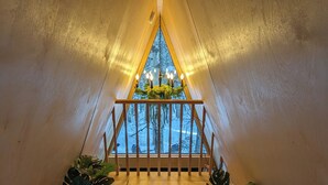 A cozy attic bedroom with a wooden floor, a chandelier, and potted plants. - The Fern A-frame Cabin (Alberta Beach)