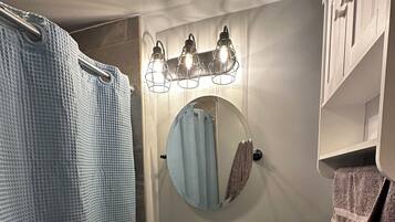 Et badeværelse med en hvid vask, toilet, bruseforhæng, et spejl og et håndklædestativ.