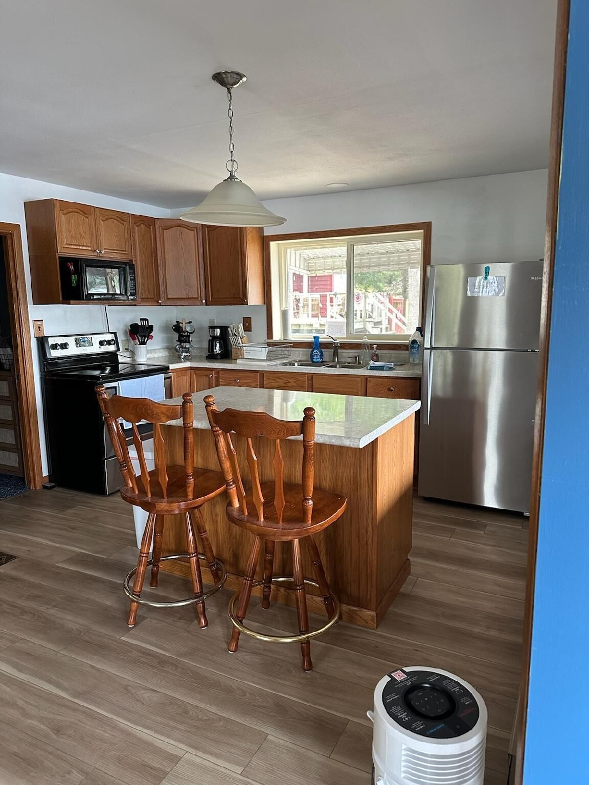 A modern kitchen with wooden cabinets, a stainless steel refrigerator, a microwave, and a gas stove. There are two wooden bar stools at the island.