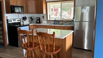 A modern kitchen with wooden cabinets, a stainless steel refrigerator, a microwave, and a gas stove. There are two wooden bar stools at the island.