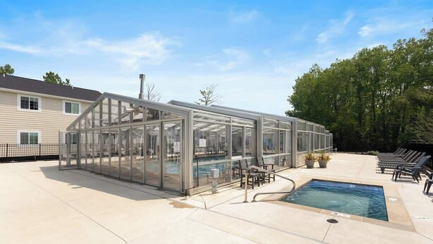 Un espace piscine entièrement vitré, offrant une vue dégagée sur la piscine, avec des chaises longues adjacentes et un bâtiment en arrière-plan.