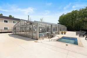A glass-enclosed pool area with a clear view of the pool, adjacent lounge chairs, and a building in the background.