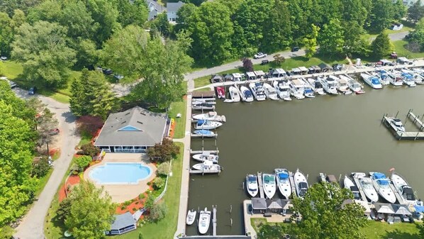 An aerial view of a marina with boats docked, a swimming pool, and a building with a sloped roof.