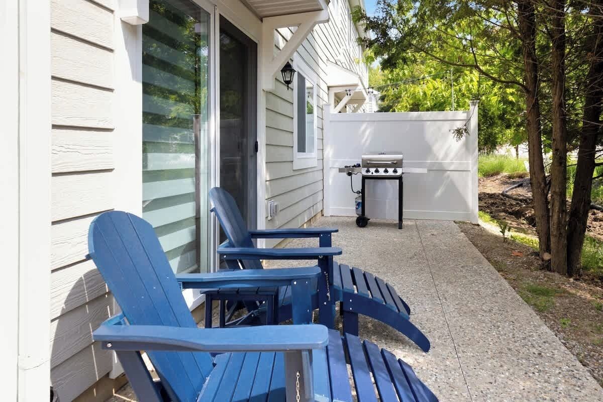 A patio with two Adirondack chairs, a grill, and a white fence.