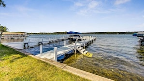 A lakeside dock with clear water, a grassy area, and a distant shoreline. - Shanahan Shores | Delavan Lakefront Cottage (Delavan)