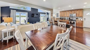 A spacious dining area with a large wooden table and white chairs, a kitchen with wooden cabinets and modern appliances, and a balcony with a view of the sea. - Shanahan Shores | Delavan Lakefront Cottage (Delavan)