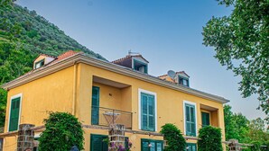 Un edificio amarillo con contraventanas verdes, una escalera de piedra y un patio cubierto de césped.