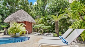 Zona piscina con lettini, una capanna con tetto di paglia e vegetazione tropicale.
