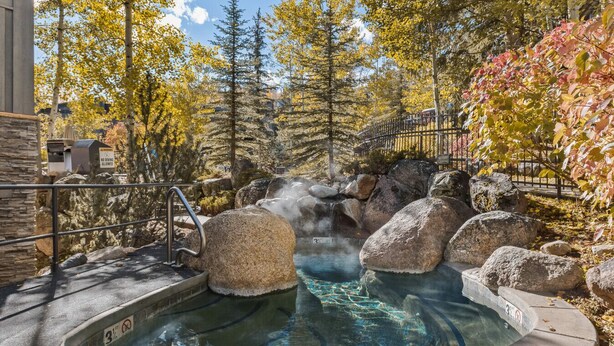 Area termale con una piscina, rocce e un cartello che vieta i tuffi.