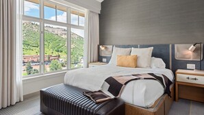 A modern hotel room with a large bed, a view of a mountainous landscape, and a wooden bench. - Luxe Resort Penthouse - Ski in Ski Out 3 Bedroom (Snowmass Village)