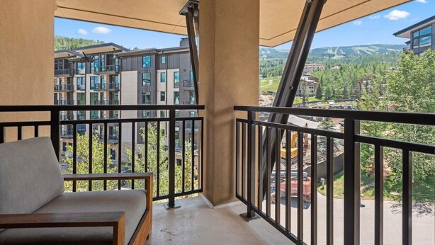 A balcony with a sofa, a view of a modern building complex, and a construction site in the background. - Luxe Resort Penthouse - Ski in Ski Out 3 Bedroom (Snowmass Village)