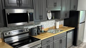 Una cocina moderna con armarios grises oscuros, electrodomésticos de acero inoxidable, encimera de madera y salpicadero de azulejos.