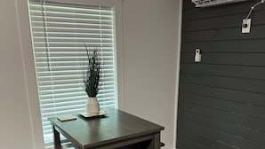 Una habitación con una mesa y un banco de madera oscura, una planta en maceta, una ventana con persianas y un aire acondicionado de pared.