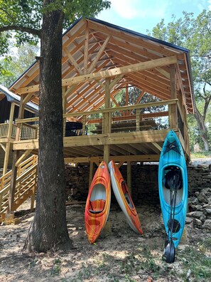 A wooden cabin with a balcony, a stone wall, and kayaks leaning against it.