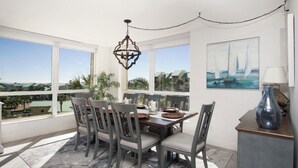A dining area with a table set for four, large windows offering a view of the landscape, and a painting on the wall. - Ocean View, Private Beach, Golf, Tennis.... (Fort Pierce)