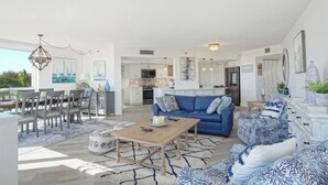 A spacious living area with a blue sofa, a wooden coffee table, and a dining set. - Ocean View, Private Beach, Golf, Tennis.... (Fort Pierce)