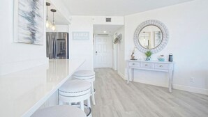 A modern, white interior with a kitchen area, a dining space with stools, and a vanity with a mirror and decorative items. - Ocean View, Private Beach, Golf, Tennis.... (Fort Pierce)