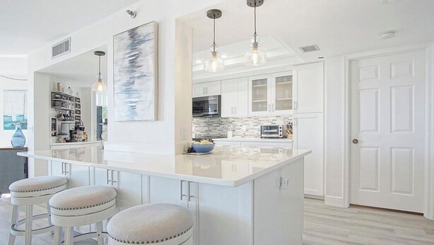 A modern kitchen with a central island, bar stools, pendant lighting, and white cabinetry. - Ocean View, Private Beach, Golf, Tennis.... (Fort Pierce)