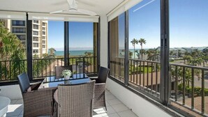 A balcony with a table and chairs, large windows with a view of the ocean and palm trees, and a ceiling fan. - Ocean View, Private Beach, Golf, Tennis.... (Fort Pierce)