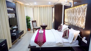 A hotel room with a large bed, a TV, a small table, a chair, and a potted plant. - hotel vikrant (Ludhiana)