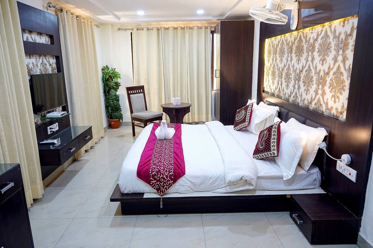 A hotel room with a large bed, a TV, a small table, a chair, and a potted plant.