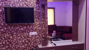 A modern bedroom with a large TV mounted on a mosaic-patterned wall, a built-in wardrobe with drawers, and a mirror cabinet. - hotel vikrant (Ludhiana)