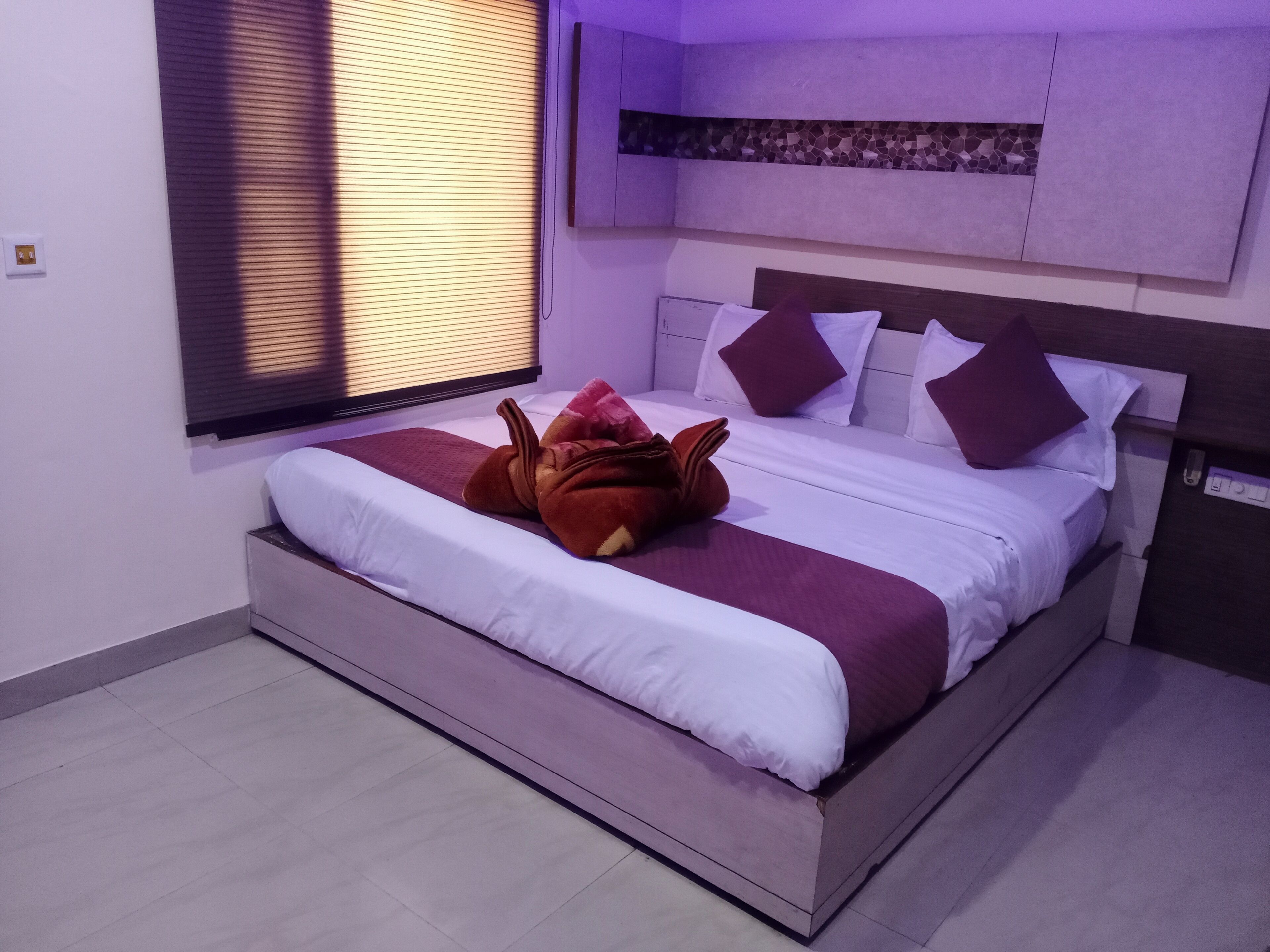 Un lit bien fait, avec une tête de lit, une fenêtre avec des stores et un panneau décoratif fixé au mur.