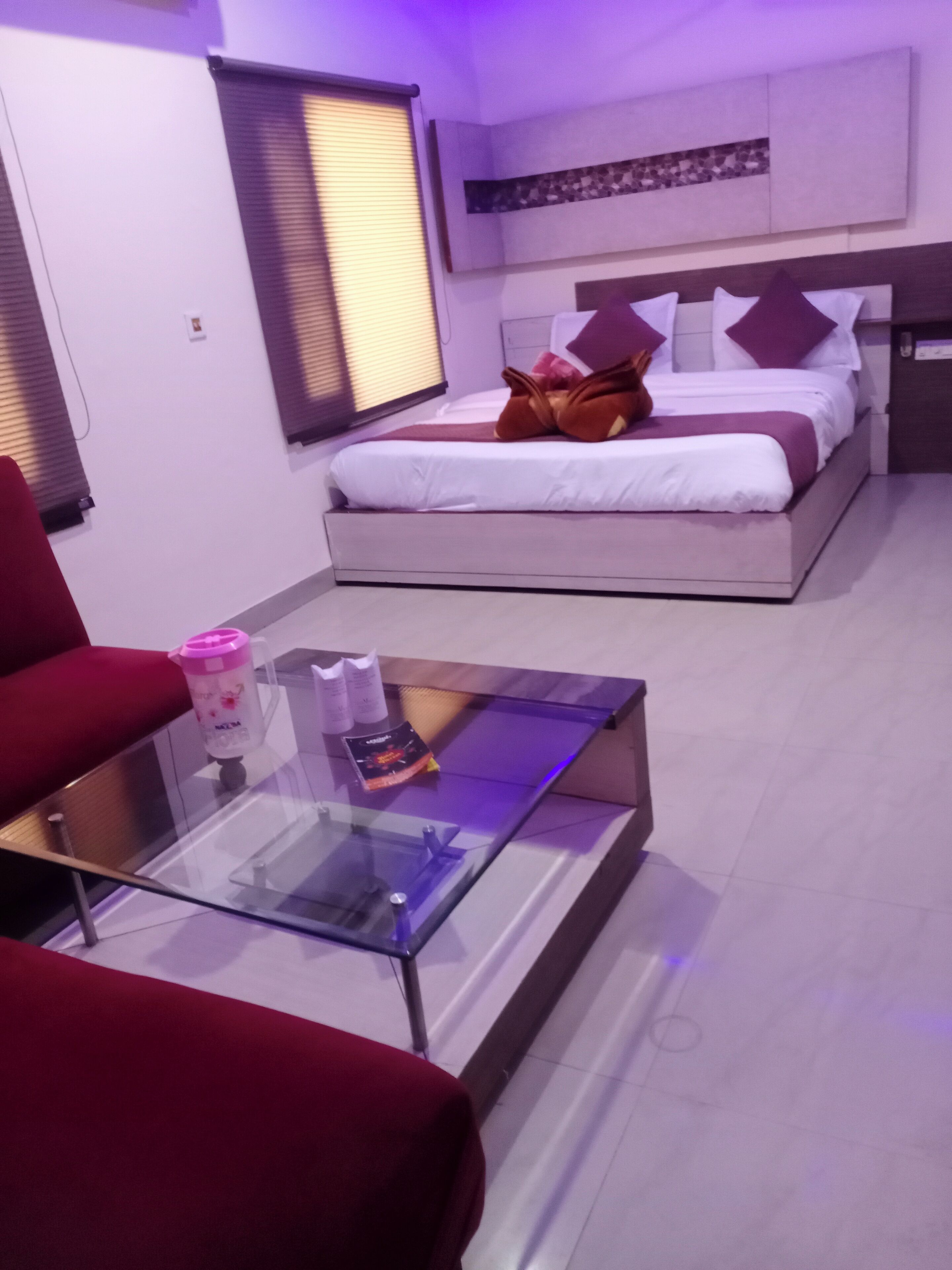 A modern bedroom with a glass coffee table, a red sofa, and a bed with white bedding and purple pillows.