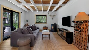 A modern living room with a wooden ceiling, a large window, a grey sofa, a TV, and a wine rack. - Ranch Retreat a mile from Warm Springs Base Lodge; New home just under an acre (Ketchum)