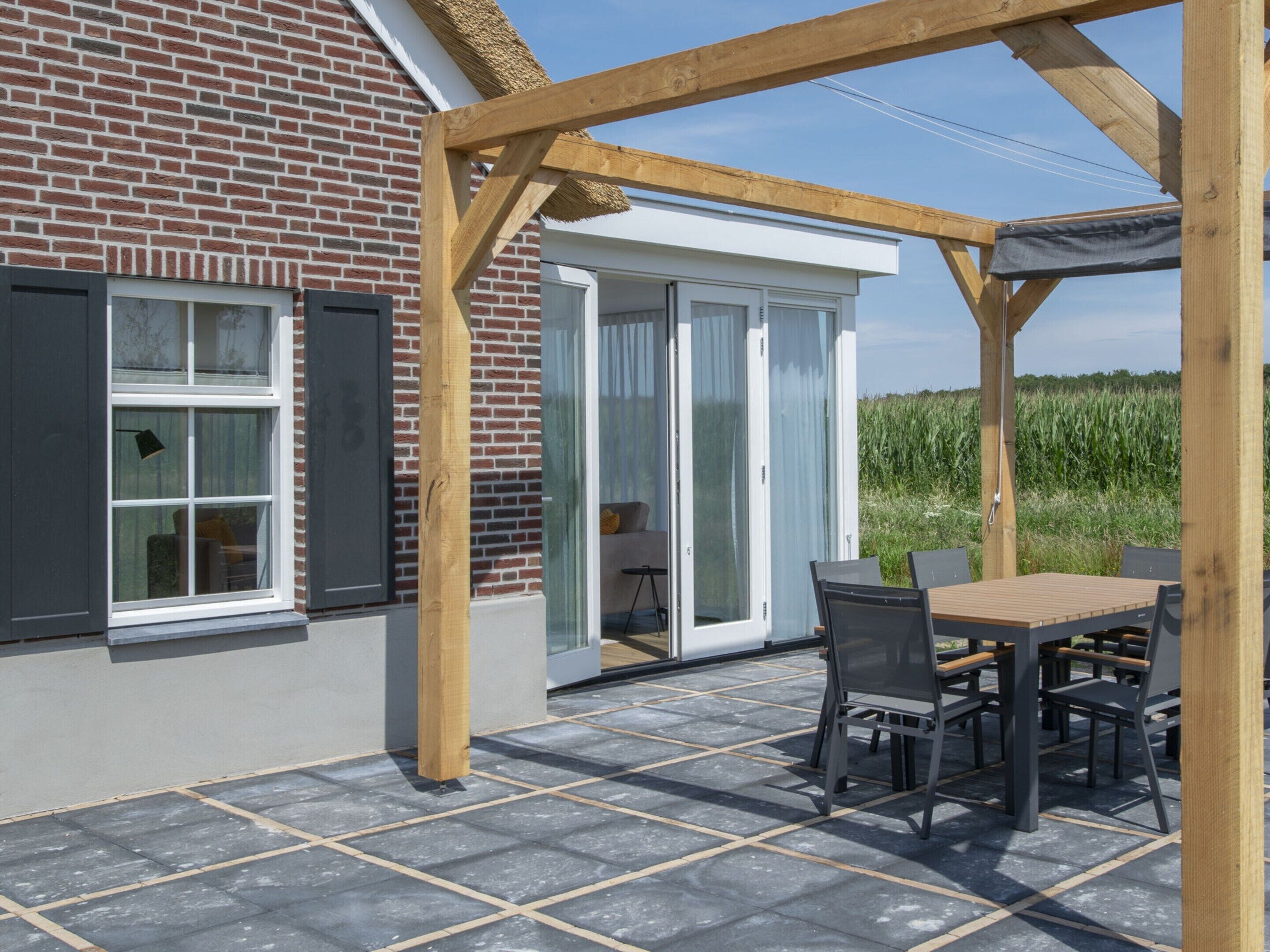 Un patio couvert avec une table et des chaises, un mur en briques et une vue sur l’extérieur.