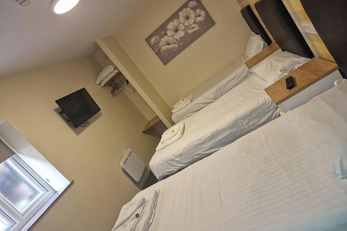 A hotel room with two beds, a flat-screen TV, a painting of flowers, and a window with blinds.