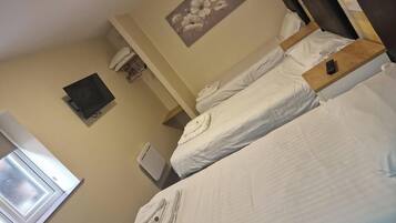 Een hotelkamer met twee bedden, een flatscreen televisie, een bloemen schilderij en een raam met zonwering.