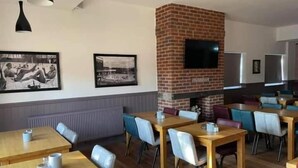 Un restaurante con mesas y sillas de madera, una chimenea de ladrillo y un televisor de pantalla plana en la pared.