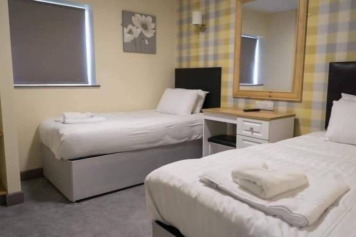 A hotel room with two beds, a desk, a mirror, and a window.