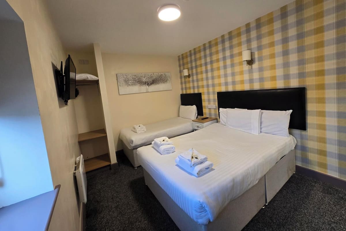 A hotel room with two beds, a checkered wall, a painting, and a flat-screen TV.