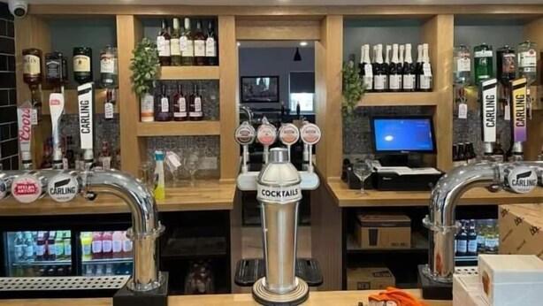 Zona de bar con varias botellas de licor, un dispensador de cócteles y una pantalla de televisión.