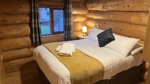 Un dormitorio tipo cabaña de madera con una cama, una mesita de noche, una lámpara y cortinas a cuadros.