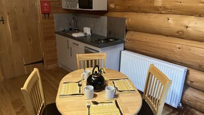 Una cabaña de madera con una mesa de comedor dispuesta para cuatro personas, una zona de cocina con microondas y una manta ignífuga en la pared.