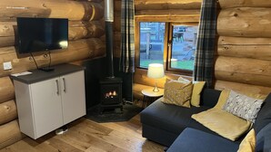 Un acogedor interior de cabaña con sofá, televisor, chimenea y ventana con cortinas.