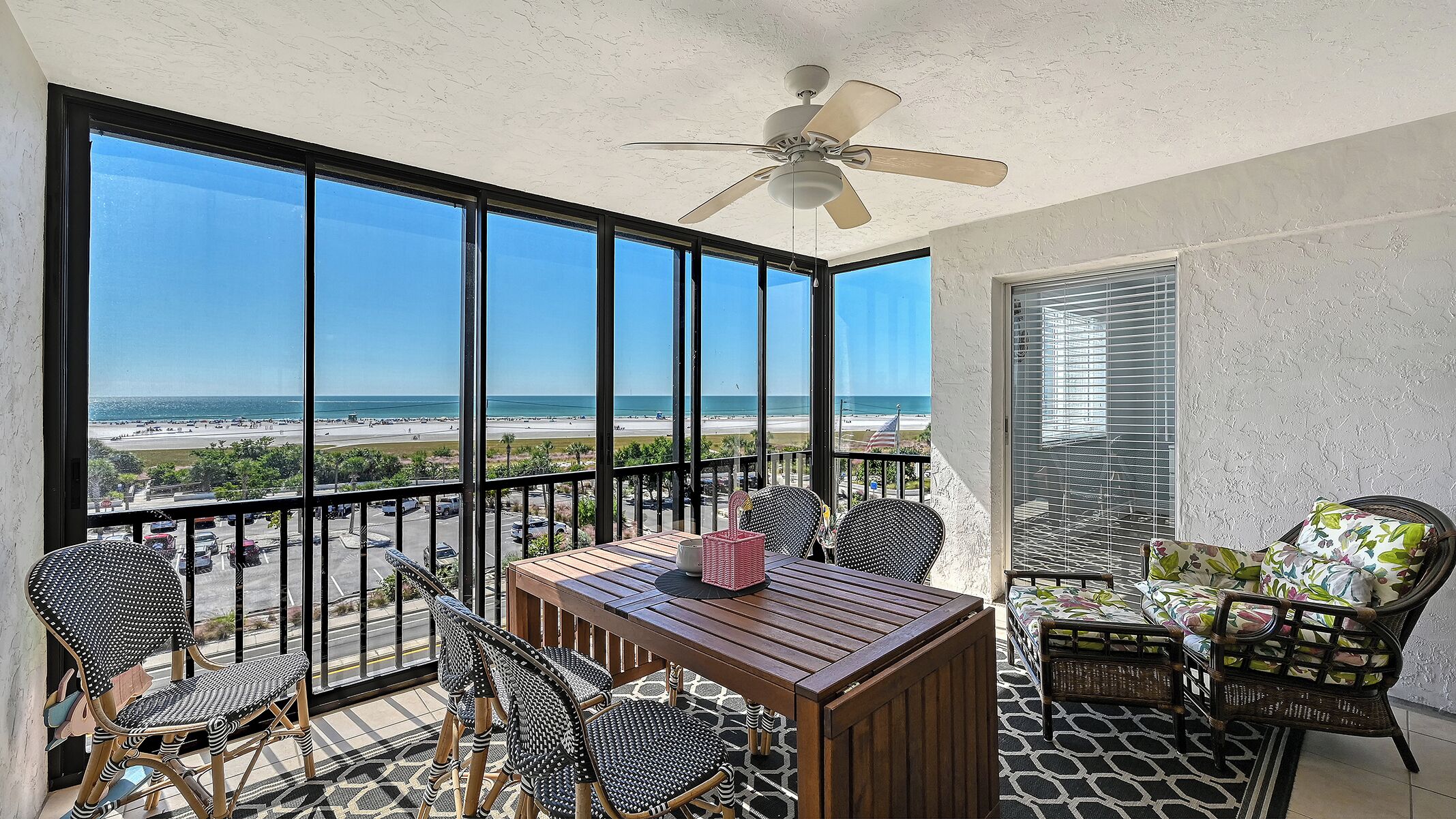 A balcony with a view of the beach, furnished with wicker chairs and a wooden table.