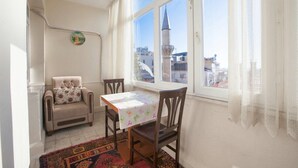 A room with a table and chairs, a window with a view of buildings and a tower, and a patterned rug on the floor. - Convenient 3-Bedroom flat for 10, Near Blue Mosque, AC & WiFi (Istanbul)